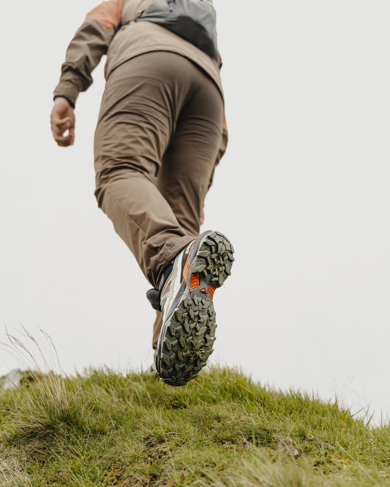 Een wandelaar in beweging, gezien vanuit een lage hoek, met de focus op de stevige, groene zolen van de wandelschoenen tegen een achtergrond van weelderig groen gras.